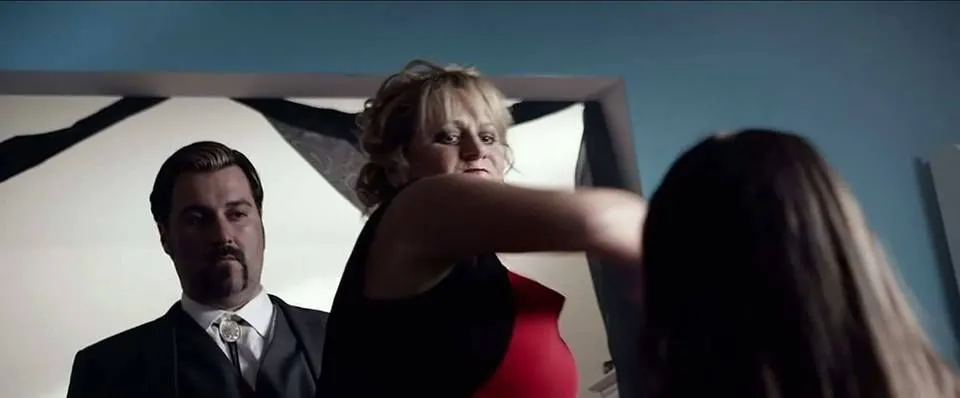 A cinematic production still of a suited performer and crew in a dim interior